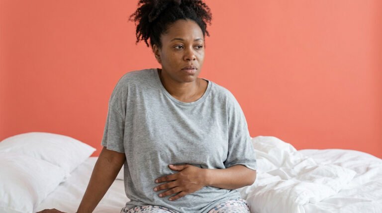 fatty liver and cholesterol — tired woman sitting on bed in the morning, hand on abdomen