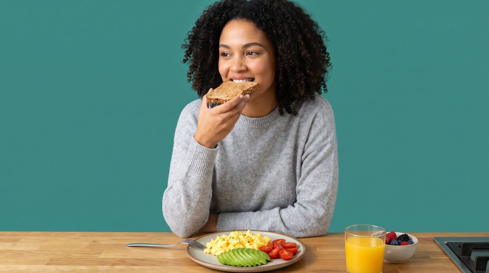 morning habits for blood sugar — woman eating balanced breakfast with eggs and avocado, teal background